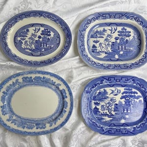 May include: Four oval ceramic platters featuring blue and white willow patterns. Two platters display detailed landscape scenes with pagodas, trees, and birds, while the other two feature decorative borders with central white areas.