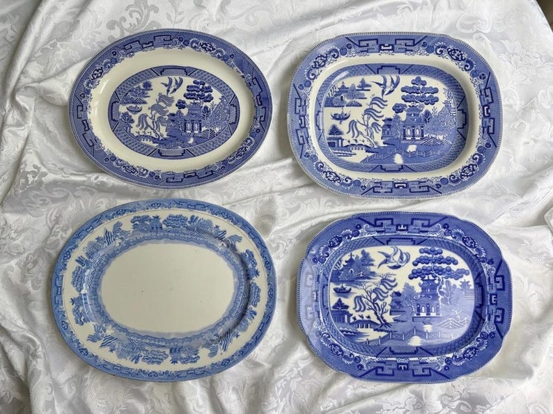 May include: Four oval ceramic platters featuring blue and white willow patterns. Two platters display detailed landscape scenes with pagodas, trees, and birds, while the other two feature decorative borders with central white areas.