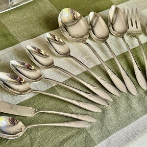 May include: A collection of nine silver-toned metal utensils including seven spoons of varying sizes, one fork, and one butter knife. Each piece features a smooth, polished finish with a subtle, tapered handle design and a simple, elegant aesthetic.