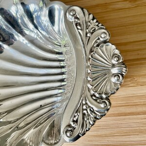 May include: A silver serving dish shaped like a seashell with ornate details. The dish is highly polished and reflects light.