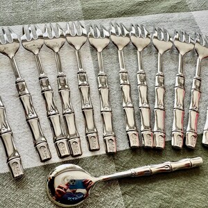 May include: A collection of silver-toned serving forks and a spoon. The forks have a bamboo-style handle design. The spoon has a round bowl and a bamboo-style handle. The items are arranged on a green and white checkered surface.