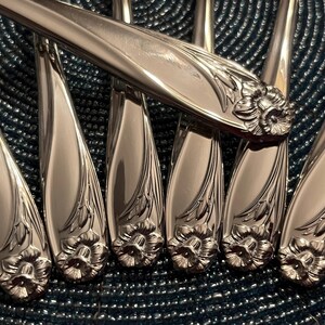 May include: A set of silver-plated dinner forks with ornate floral designs. The forks have a polished finish and are arranged in a fan shape.