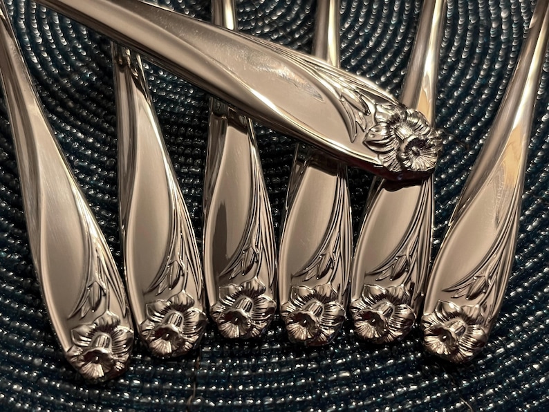 May include: A set of silver-plated dinner forks with ornate floral designs. The forks have a polished finish and are arranged in a fan shape.