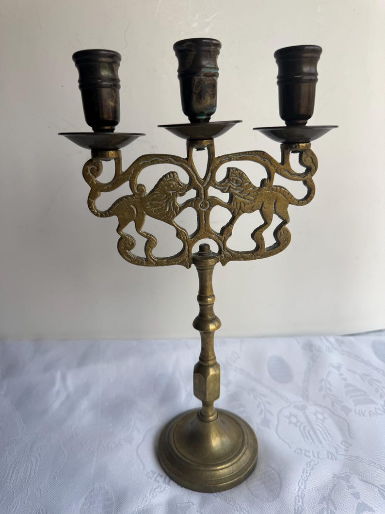 Pu&ograve; includere: Un candelabro in ottone con tre portacandele. Il pezzo decorativo presenta due figure di leone sul davanti. La base &egrave; rotonda e l'altezza totale &egrave; di circa 25 cm.