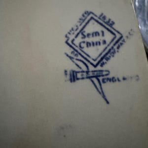 May include: A cream-colored ceramic surface featuring a dark blue stamped maker's mark. The mark includes a diamond shape with the text Semi China, the number 1632, the name W. Ridgway & Co, and the word England, accompanied by a small graphic icon.