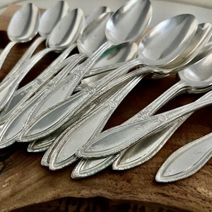 K&ouml;nnte beinhalten: Ein Set vintage Silberl&ouml;ffel mit verzierten Griffen. Die L&ouml;ffel sind gestapelt und auf einer Holzoberfl&auml;che angeordnet.