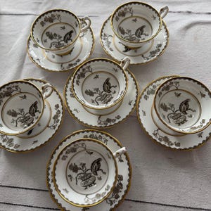 May include: Set of six teacups and saucers with a black and white floral design. The cups and saucers have a gold trim.