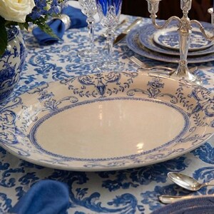 K&ouml;nnte beinhalten: Eine ovale Servierplatte mit cremefarbenem Mittelteil und blauem Blumenrand. Die Platte ist Teil einer Tischdekoration mit anderem blau-wei&szlig;em Porzellan, Kristallgl&auml;sern und einem Blumengesteck.