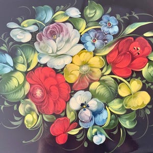 May include: A decorative tray with a dark background, featuring a vibrant floral arrangement. The flowers include red, yellow, white, and blue blooms with green leaves. The tray's edge has a gold trim.