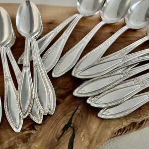 May include: A set of silver teaspoons with ornate handles, arranged on a wooden surface.