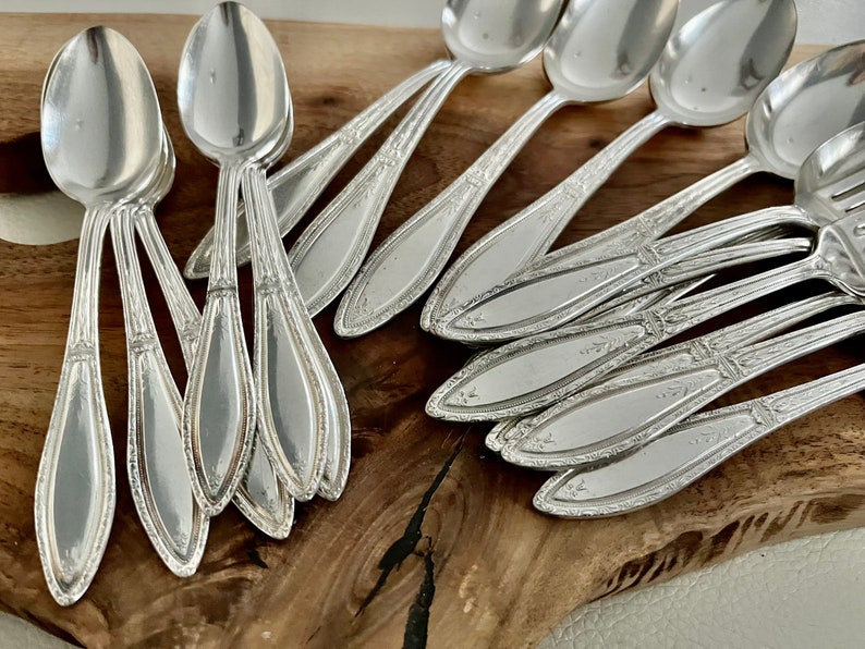 May include: A set of silver teaspoons with ornate handles, arranged on a wooden surface.