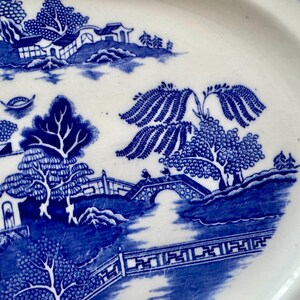 K&ouml;nnte beinhalten: Blau-wei&szlig;es Weidenmuster auf einem Keramikteller. Das Muster zeigt eine Br&uuml;cke, B&auml;ume und einen Pagodentempel.