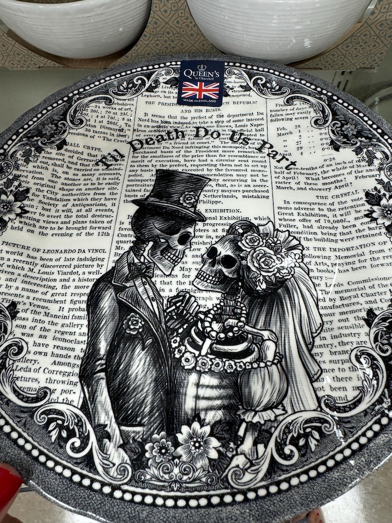 K&ouml;nnte beinhalten: Schwarzer und wei&szlig;er Keramik-Dinnerteller mit einem gotischen Design, das zwei Skelette in Hochzeitskleidung zeigt. Der Teller hat einen dekorativen Rand und einen Text&uuml;berlagerung mit den Worten "Til Death Do Us Part".