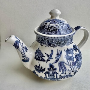 K&ouml;nnte beinhalten: Eine wei&szlig;e Teekanne mit einem blauen und wei&szlig;en Weidenmuster. Die Teekanne hat einen runden K&ouml;rper und einen Deckel mit einem Knopf oben. Die Teekanne ist mit einem traditionellen chinesischen Design verziert.