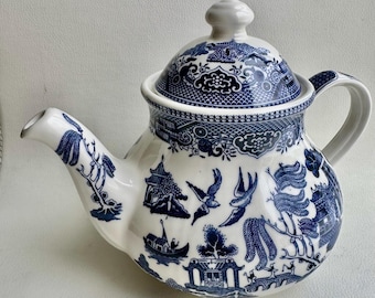 May include: A white teapot with a blue and white willow pattern. The teapot has a round body and a lid with a knob on top. The teapot is decorated with a traditional Chinese design.