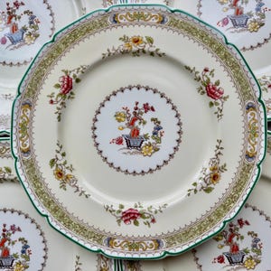 Puede incluir: Juego de cinco platos de cena de cer&aacute;mica blanca con un dise&ntilde;o floral verde, dorado y floral. Cada plato presenta un motivo floral central con una planta en maceta y un borde delicado.