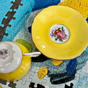 Pu&ograve; includere: Un set composto da tazza da t&egrave; e piattino di colore giallo brillante. Il piattino presenta un medaglione centrale bianco con un bouquet di fiori rosa, rossi e viola. La base della tazza mostra un marchio con il testo Mason's e Made in England.