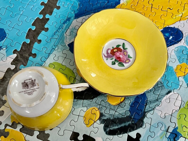 Pu&ograve; includere: Un set composto da tazza da t&egrave; e piattino di colore giallo brillante. Il piattino presenta un medaglione centrale bianco con un bouquet di fiori rosa, rossi e viola. La base della tazza mostra un marchio con il testo Mason's e Made in England.