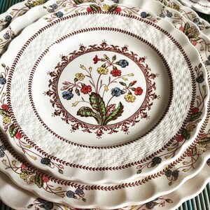 Op de afbeelding: Een set van drie witte keramische borden met een bruin en rood bloemenmotief. De borden hebben een gegolfde rand en een geweven patroon.