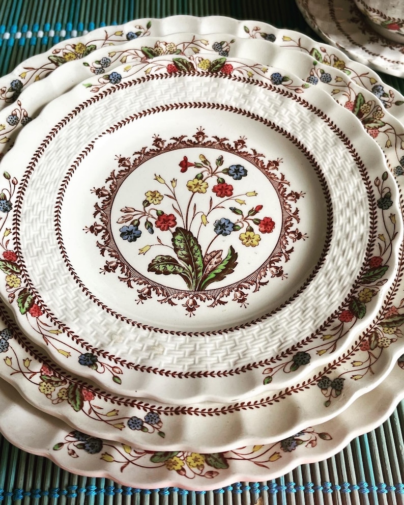 Op de afbeelding: Een set van drie witte keramische borden met een bruin en rood bloemenmotief. De borden hebben een gegolfde rand en een geweven patroon.