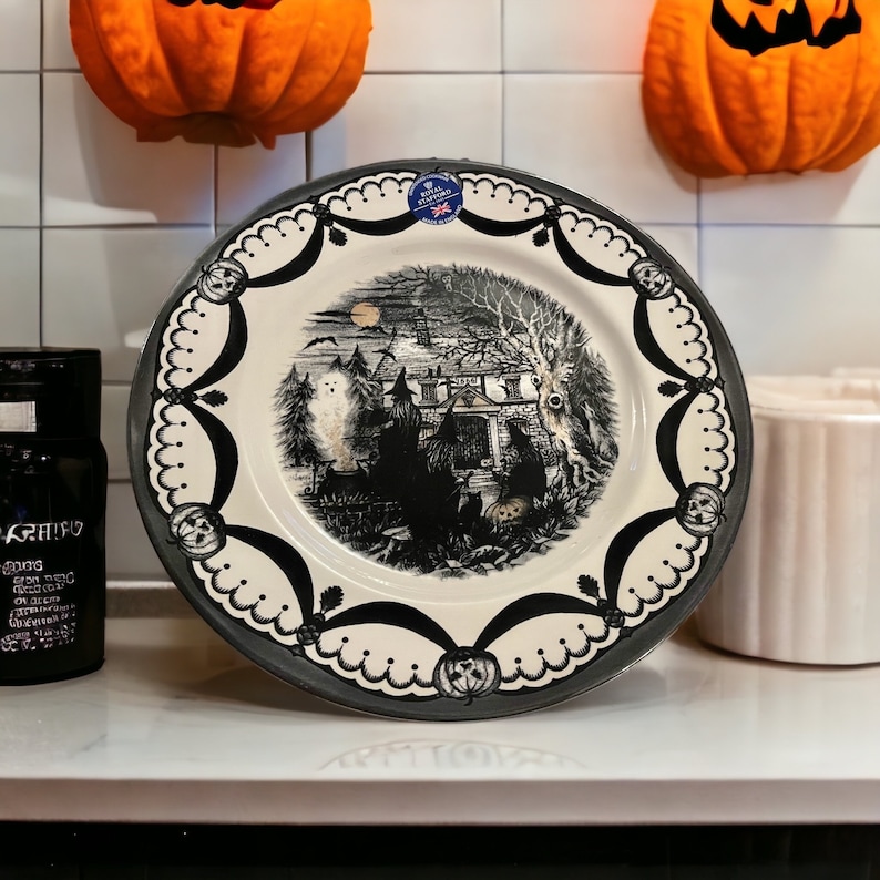 K&ouml;nnte beinhalten: Ein schwarzer und wei&szlig;er Keramik-Dinnerteller mit einer gruseligen Halloween-Szene mit einem Spukhaus, B&auml;umen und einem Geist. Der Teller hat einen schwarzen und wei&szlig;en gewellten Rand mit einem schwarzen Bandmuster.