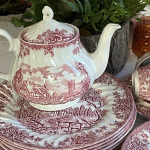 May include: A white teapot with a pink and red floral design. The teapot is sitting on a pink and white floral patterned plate.