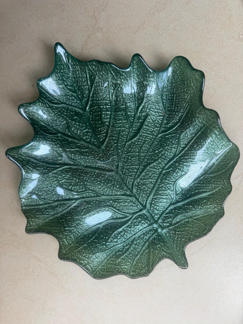 Puede incluir: Un cuenco de cristal verde oscuro con forma de hoja grande y superficie texturizada que imita las venas naturales y los contornos org&aacute;nicos. El cuenco presenta un acabado brillante y bordes irregulares festoneados que siguen la silueta de una hoja.