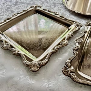 Puede incluir: Un juego de tres bandejas de metal plateado que incluye una bandeja cuadrada, una rectangular y una redonda. Cada bandeja tiene una superficie reflectante con un patr&oacute;n floral grabado y un borde elevado, ornamentado y festoneado.