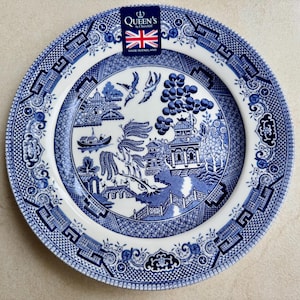 May include: A round ceramic plate featuring a blue and white willow pattern with a central scene of a pagoda, a bridge, and birds. A rectangular label at the top displays the text Queen's by Churchill with a Union Jack and Made in England.