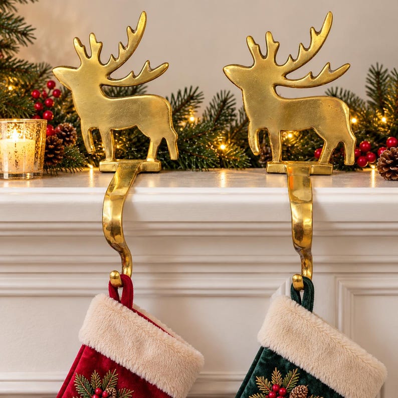 May include: Two gold-toned metal reindeer stocking holders with curved hooks. Each holder features a standing reindeer silhouette with antlers. The hooks extend downward to support a red stocking and a dark green stocking, both with white faux fur cuffs.