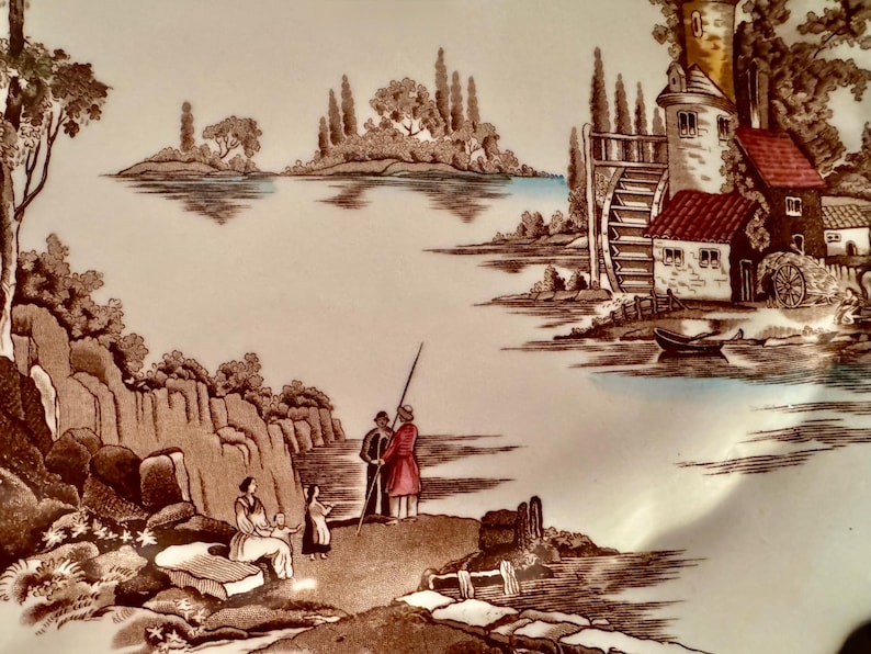 Op de afbeelding: Een keramieken bord met een sepia-kleurige landschapsillustratie van een watermolen, een stenen toren en een meer met eilanden. Op de voorgrond staan figuren bij rotsachtige kliffen en een kleine boot in bruin, wit en blauw.