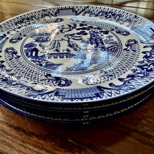 K&ouml;nnte beinhalten: Ein Stapel blau-wei&szlig;er Porzellanteller. Jeder Teller zeigt ein detailliertes, traditionelles, asiatisch inspiriertes Design mit Pagoden, Br&uuml;cken und floralen Mustern. Die Teller sind ordentlich gestapelt und pr&auml;sentieren die komplizierten Kunstwerke und die tiefblaue Farbe.