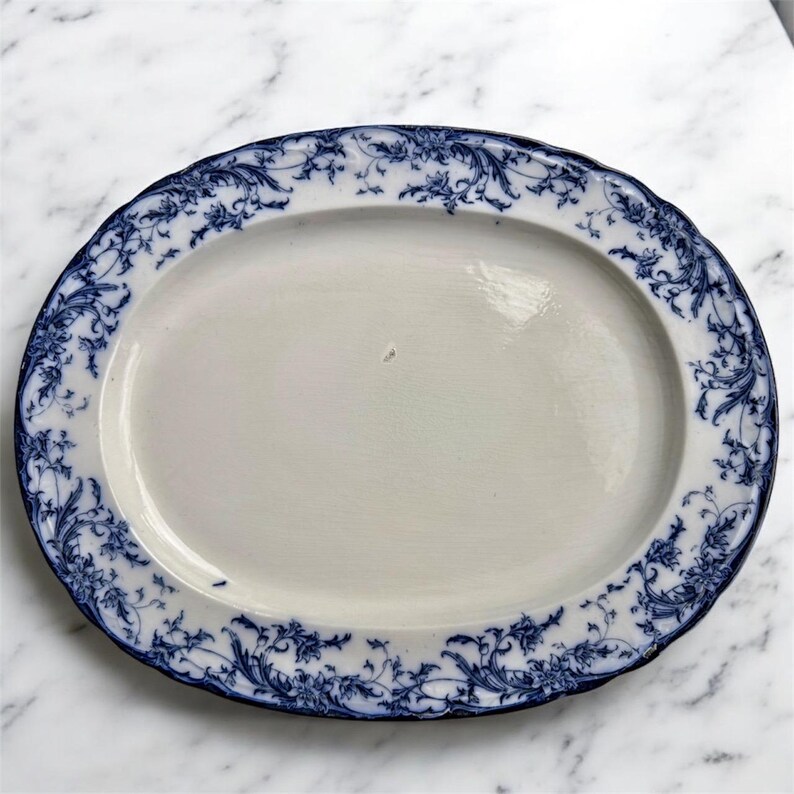 Puede incluir: Plato ovalado para servir con centro blanco y borde floral azul. El borde presenta un borde festoneado. El dise&ntilde;o azul es un patr&oacute;n detallado y repetitivo de hojas y vides. El plato es de cer&aacute;mica.