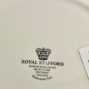 Może przedstawiać: Biały ceramiczny talerz z czarno-białym logo Royal Stafford. Logo zawiera koronę i tekst "Royal Stafford" oraz "Made in Burslem the heart of the potteries England Dishwasher Safe".
