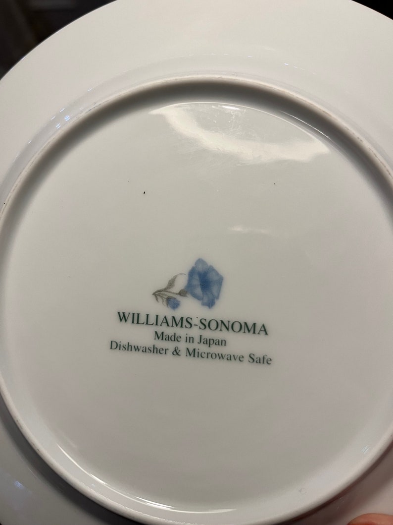 K&ouml;nnte beinhalten: Wei&szlig;e Keramikplatte mit blauem Blumendesign und dem Text "WILLIAMS-SONOMA Made in Japan Dishwasher & Microwave Safe". Die Platte hat eine gl&auml;nzende Oberfl&auml;che.