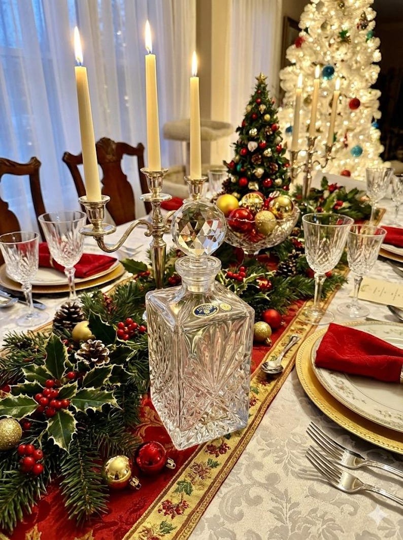May include: A festive Christmas table setting with a crystal decanter, lit candles, and a small Christmas tree. The table is decorated with holly, ornaments, and gold accents. Wine glasses and plates are set for a holiday meal.