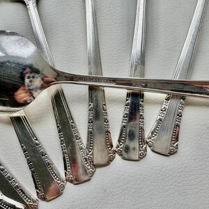 May include: A set of eight silver spoons with ornate designs. The spoons are arranged in a fan shape, with the handles overlapping.