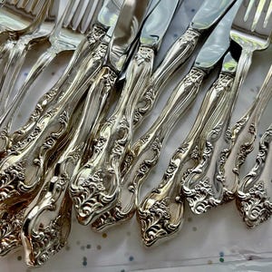 May include: A collection of ornate silver forks and knives. The silverware features a detailed floral pattern on the handles and a shiny, reflective surface. The arrangement suggests a formal dining setting, perfect for special occasions.