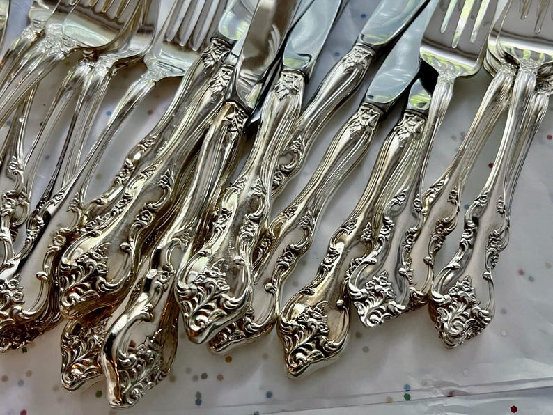 May include: A collection of ornate silver forks and knives. The silverware features a detailed floral pattern on the handles and a shiny, reflective surface. The arrangement suggests a formal dining setting, perfect for special occasions.