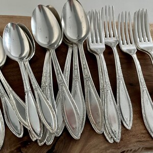May include: A set of silver-plated spoons and forks with ornate designs. The silverware is arranged on a wooden surface.