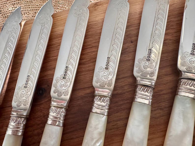Pu&ograve; includere: Set di sei coltelli d'argento con manici in madreperla. Le lame sono incise con un motivo floreale e i manici hanno una fascia d'argento con l'iscrizione "BOGGE" su ciascuno.