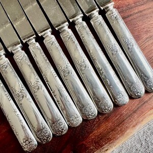 May include: A set of ten silver-plated dinner knives with ornate floral designs on the handles.