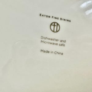 May include: Close-up of a white ceramic plate with the text "EATON FINE DINING" and a logo. Below the logo, it reads "Dishwasher and Microwave safe" and "Made in China".