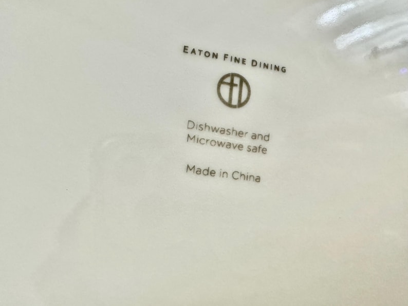 May include: Close-up of a white ceramic plate with the text "EATON FINE DINING" and a logo. Below the logo, it reads "Dishwasher and Microwave safe" and "Made in China".