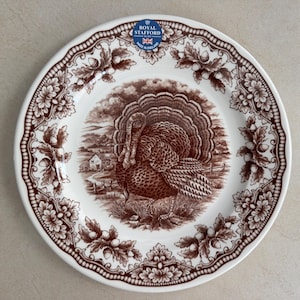 Op de afbeelding: Een wit keramieken bord met een bruin transferware patroon van een kalkoen in een landelijk landschap. De rand is versierd met een ingewikkelde rand van eikenbladeren en eikels. Een blauw-wit Royal Stafford Made in England label is aanwezig.