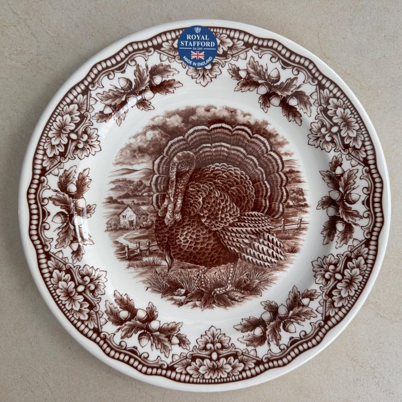Op de afbeelding: Een wit keramieken bord met een bruin transferware patroon van een kalkoen in een landelijk landschap. De rand is versierd met een ingewikkelde rand van eikenbladeren en eikels. Een blauw-wit Royal Stafford Made in England label is aanwezig.