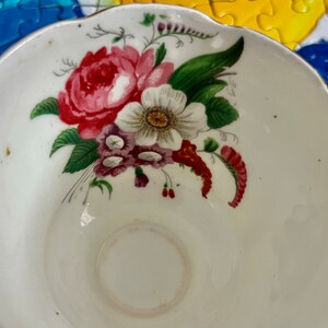 Pu&ograve; includere: Una tazza da t&egrave; in porcellana bianca con bordo smerlato e finitura color oro. L'interno della tazza &egrave; decorato con un'illustrazione colorata di un bouquet di fiori, che include una grande rosa rossa, un fiore bianco e foglie verdi.