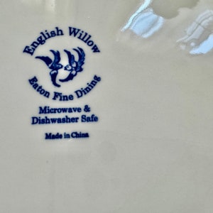 K&ouml;nnte beinhalten: Nahaufnahme eines wei&szlig;en Keramiktellers mit den Worten "English Willow Eaton Fine Dining" in Blau. Der Teller ist mikrowellen- und sp&uuml;lmaschinenfest, hergestellt in China.