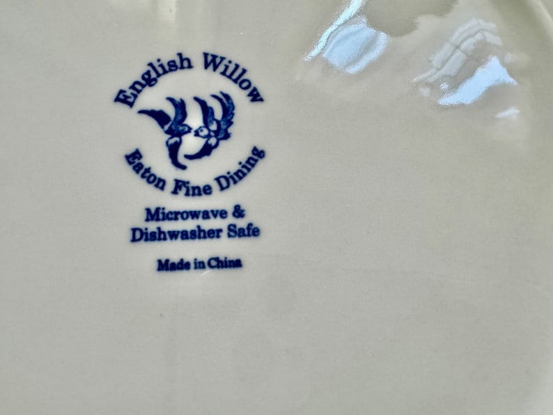 K&ouml;nnte beinhalten: Nahaufnahme eines wei&szlig;en Keramiktellers mit den Worten "English Willow Eaton Fine Dining" in Blau. Der Teller ist mikrowellen- und sp&uuml;lmaschinenfest, hergestellt in China.
