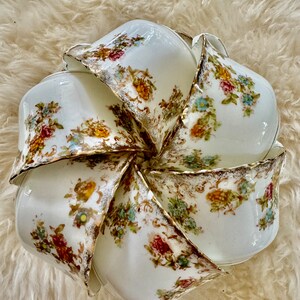 K&ouml;nnte beinhalten: Ein Set aus acht wei&szlig;en Porzellan-Teetassen mit floralem Muster und goldener Verzierung. Die Tassen sind in einem Kreis angeordnet, wobei die R&auml;nder der Tassen nach au&szlig;en zeigen.